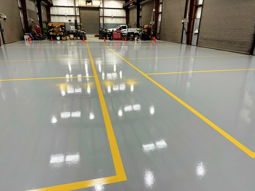 Glossy gray Resinous 123 epoxy coating with safety-yellow line striping in an industrial warehouse bay with roll-up doors and work trucks