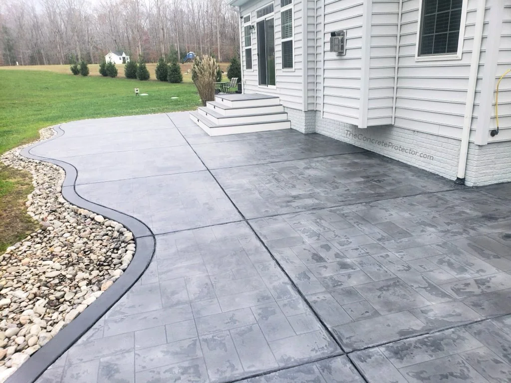 Tuscan Slate backyard patio in an ashlar tile layout, edged with river rock